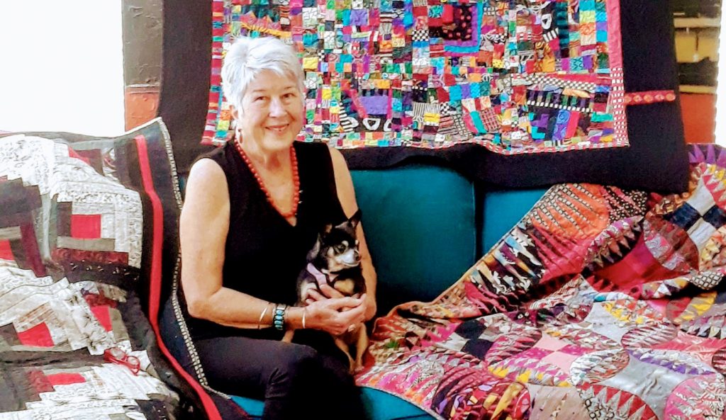 Diane Magrina holding her cat surrounded by quilts