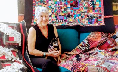 Diane Magrina holding her cat surrounded by quilts