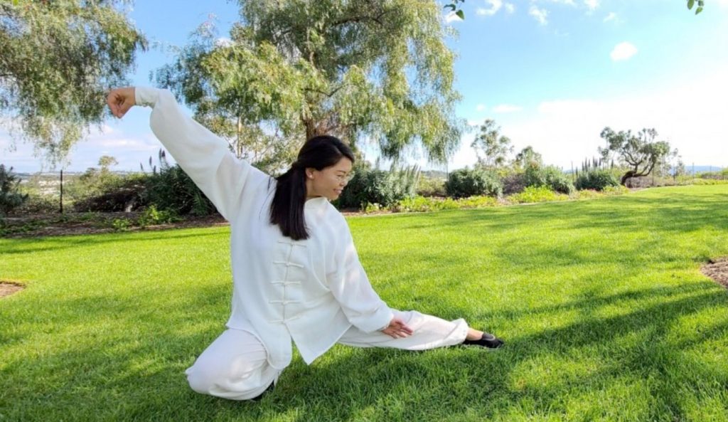 female in white practicing taichi on grassy land
