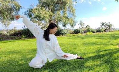 Dr. Hui Hwang in white practicing Tai Chi on grass