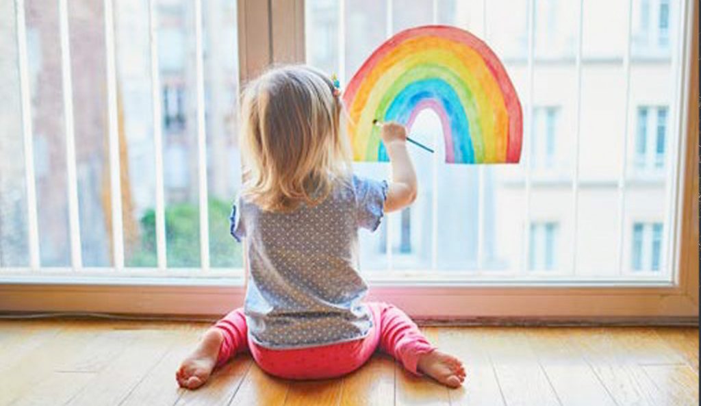child sitting at the window drawing rainbow on the glass