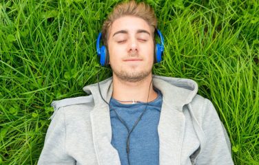 young man laying in grass relaxing - biofeedback relaxation